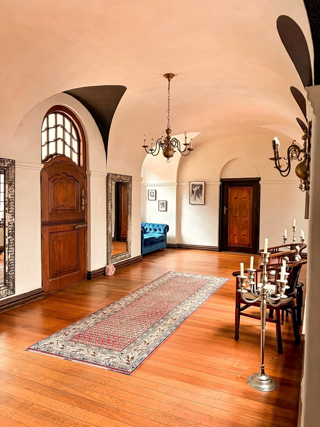 An arched hallway inside the manor with chandeliers and Persian rugs
